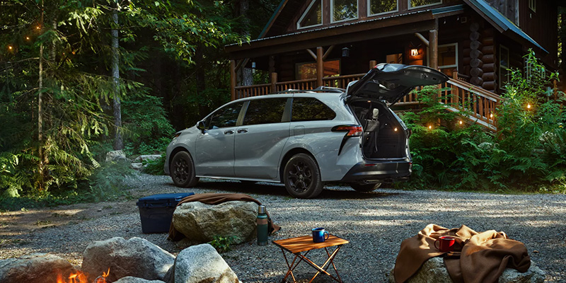 A Toyota sienna with it's trunk open, parked in front of a cabin.