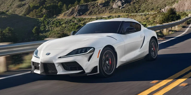 A white 2025 Toyota GR Supra driving down the road.
